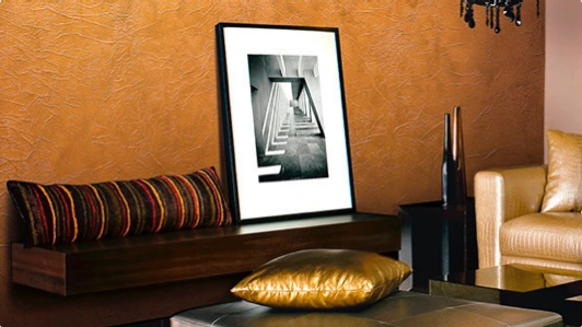 A living room with a sofa, table and painting in front of a bronze texture wall.