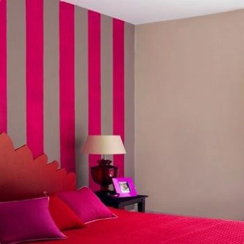 A bedroom with pink and grey wallpaper and a pink bed. Furnishings by Asian Paints.