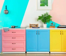 Pink, Blue, and Yellow Cupboard with decor on top of it in front of a colourful wall. Wood & Metal Painting Services by Asian Paints.