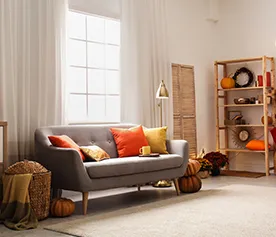 A grey 3-seater sofa decorated with orange and yellow cushions. 10 ideas to decorate the living room on a budget blog.