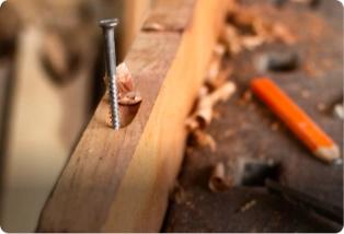 A wooden plank with a partially driven screw, surrounded by wood shavings, a pencil, and carpentry tools. Carpenters for your home trusted by Asian Paints.