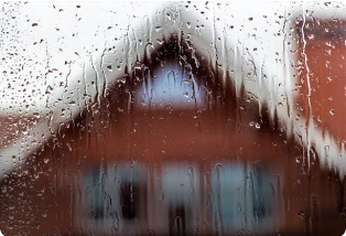 A window pane covered with raindrops foreshadowing the view of a home. Waterproofing contractors for your home.